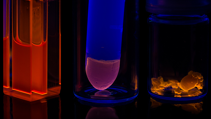 Orangefarbig fluoreszierende kolloidale Nanopartikeln in Küvette (links), Hydrogel mit schwächerer Fluoreszenz der gleichen Nanopartikel ind Eppendorff Tube (Mitte), Aerogel dieser Nanopartikel, orangefarbige Fluoreszenz (rechts)